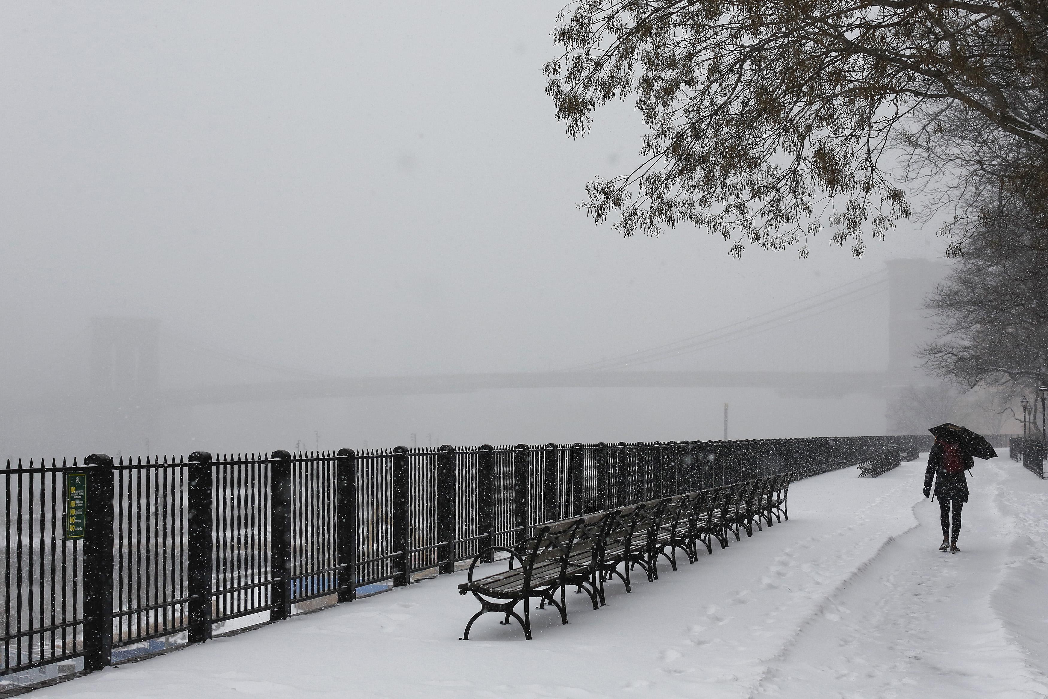 A woman walks with an umbrella along the Brooklyn Promenade during snow fall in New York